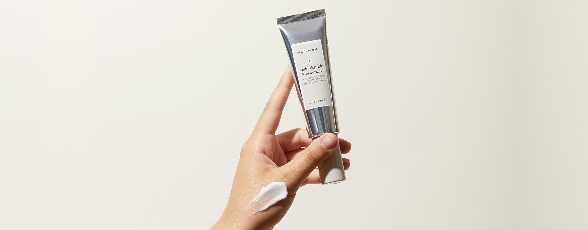 a hand holds up a tube of multi-peptide moisturizer. 